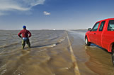 A man looks out over massively flooded road and farmland